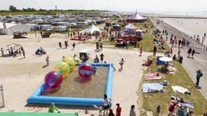 Una playa con área de juegos acuáticos inflables, tiendas de campaña y gente.
