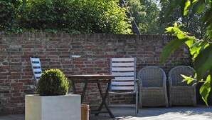 A patio with a brick wall, a table, two wicker chairs, and a planter with a small tree. - Studio apartment in restored captain's house with a panoramic view of the port (Krummhörn)