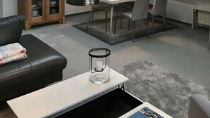 A modern living room with a dining area, featuring a loft-style ceiling, a wooden cabinet, a black leather sofa, and a glass table with a candle. - Studio apartment in restored captain's house with a panoramic view of the port (Krummhörn)