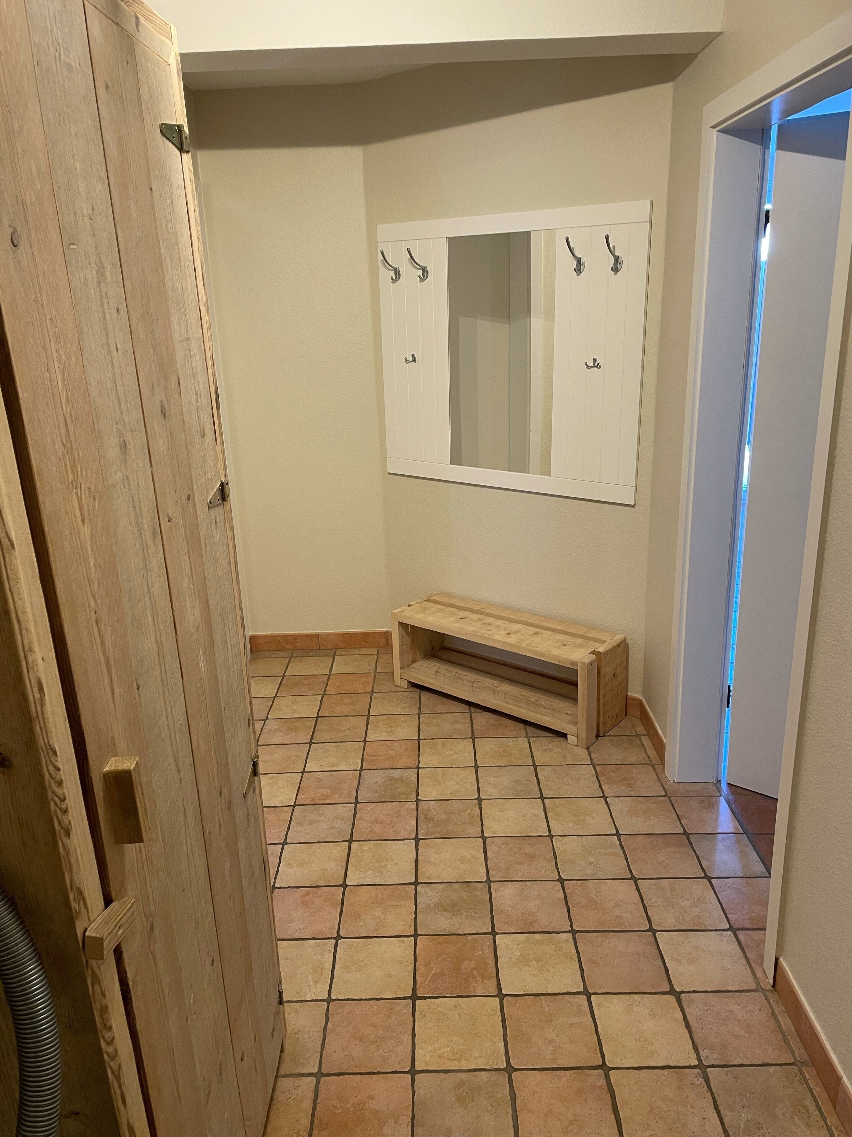 A hallway with a wooden bench, a white door with a mirror, and a tiled floor.