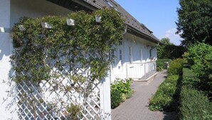 A white building with a sloped roof and a lattice wall covered in climbing plants. - September 8–21: Off! Cozy vacation rental with a balcony, 2 bedrooms, and a parking space in Grömitz (Grömitz)