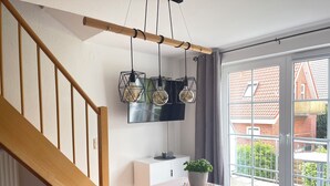 A modern interior with a staircase, a dining area with a table and chairs, a potted plant, and a view of a red-brick building through a glass door. - September 8–21: Off! Cozy vacation rental with a balcony, 2 bedrooms, and a parking space in Grömitz (Grömitz)
