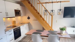 A modern kitchen with white cabinets, a wooden staircase, and a dining area with a table and chairs. - September 8–21: Off! Cozy vacation rental with a balcony, 2 bedrooms, and a parking space in Grömitz (Grömitz)