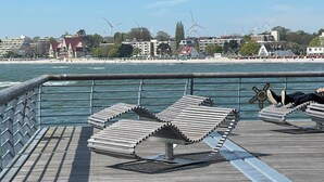 A wooden pier with metal railings, overlooking a beach with wind turbines in the background. - September 8–21: Off! Cozy vacation rental with a balcony, 2 bedrooms, and a parking space in Grömitz (Grömitz)