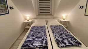 A narrow room with two beds, each with a striped blanket, and two bedside lamps.