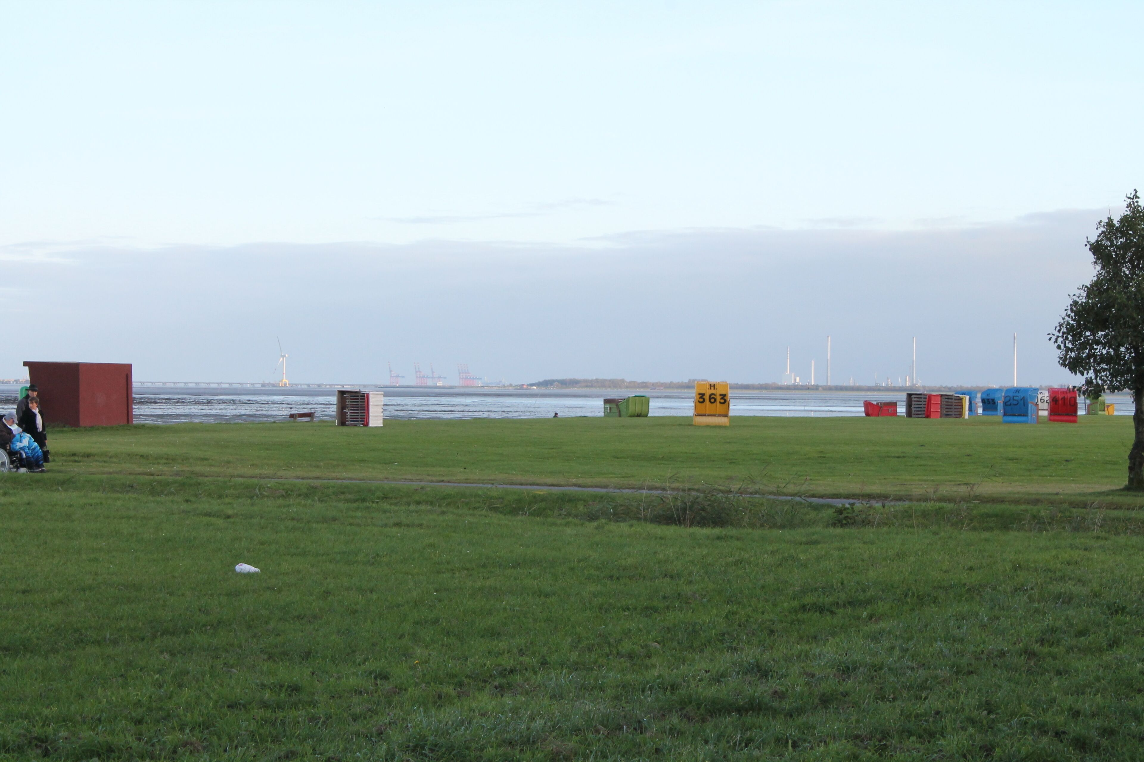Een grasveld met een waterlichaam op de achtergrond, een windmolen en een verre kustlijn met gebouwen.