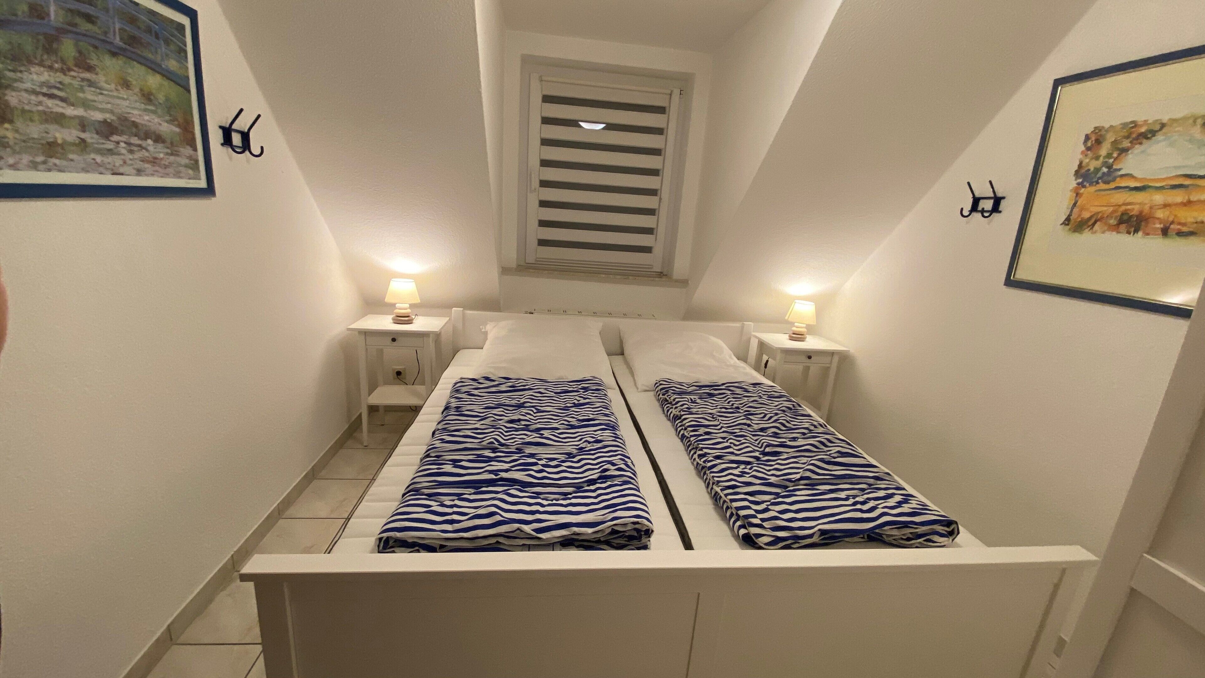 A narrow room with two beds, each with a striped blanket and a bedside lamp.