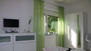 Une chambre à coucher avec un lit, une commode, un téléviseur et une fenêtre avec des rideaux.