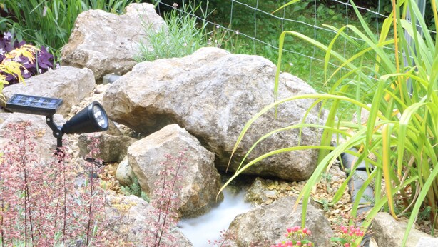 Un jardin agrémenté de gros rochers, d’un élément décoratif aquatique et d’un éclairage extérieur alimenté par énergie solaire.