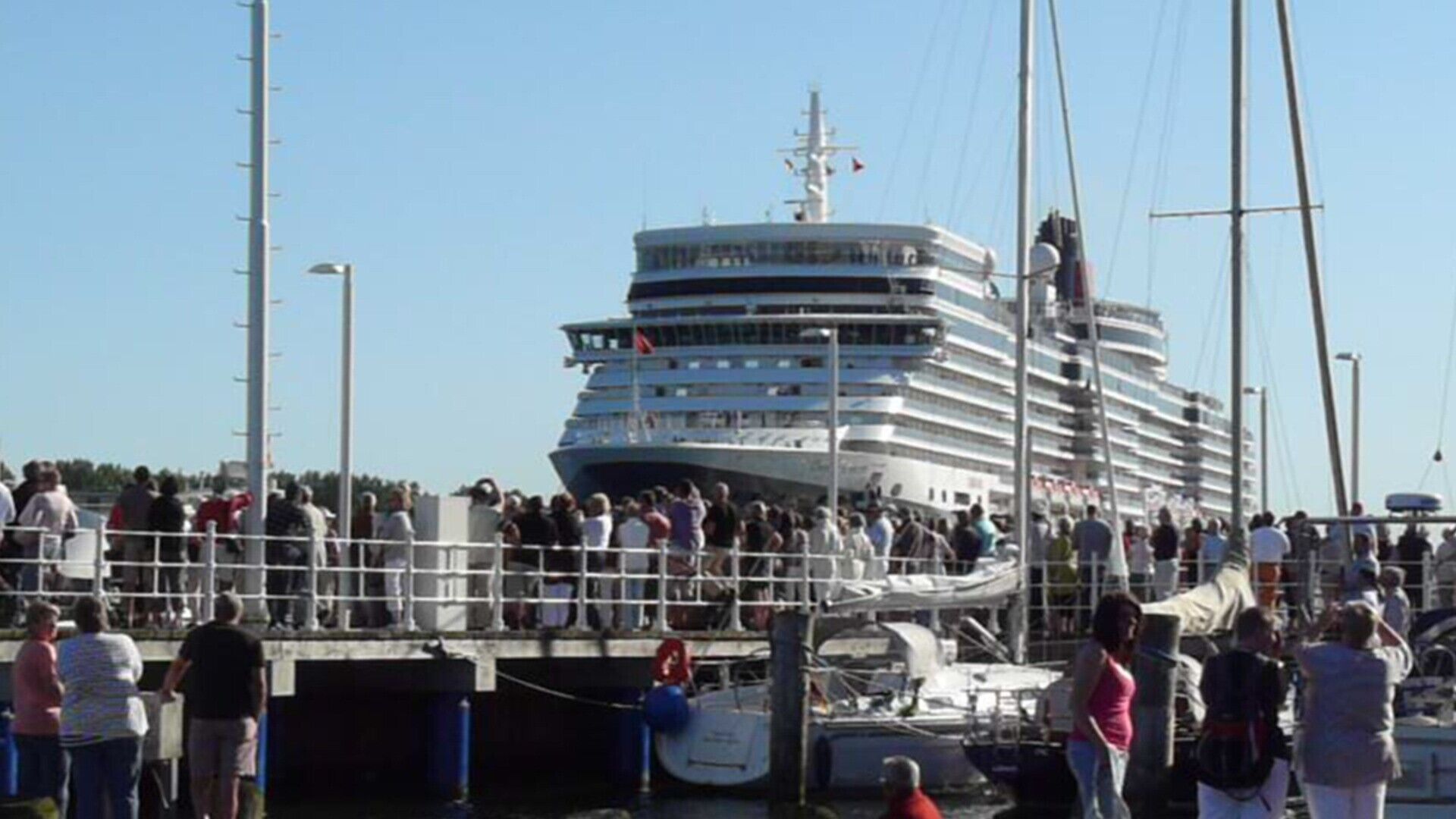 A large cruise ship docked at a port with a crowd of people gathered around it.