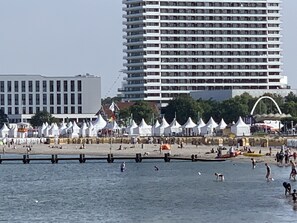 A beach with white tents and people swimming. There are tall buildings in the background.