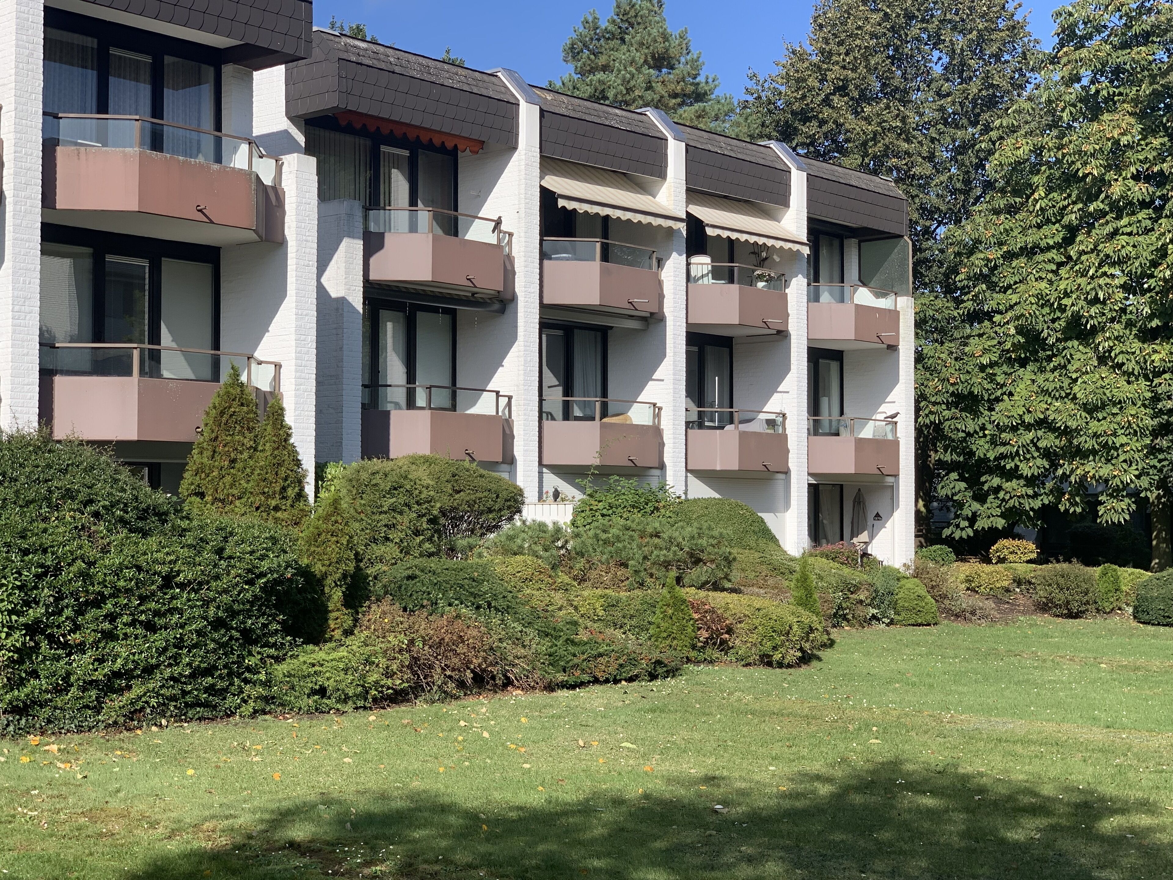A multi-story residential building with balconies, surrounded by well-maintained hedges and trees.