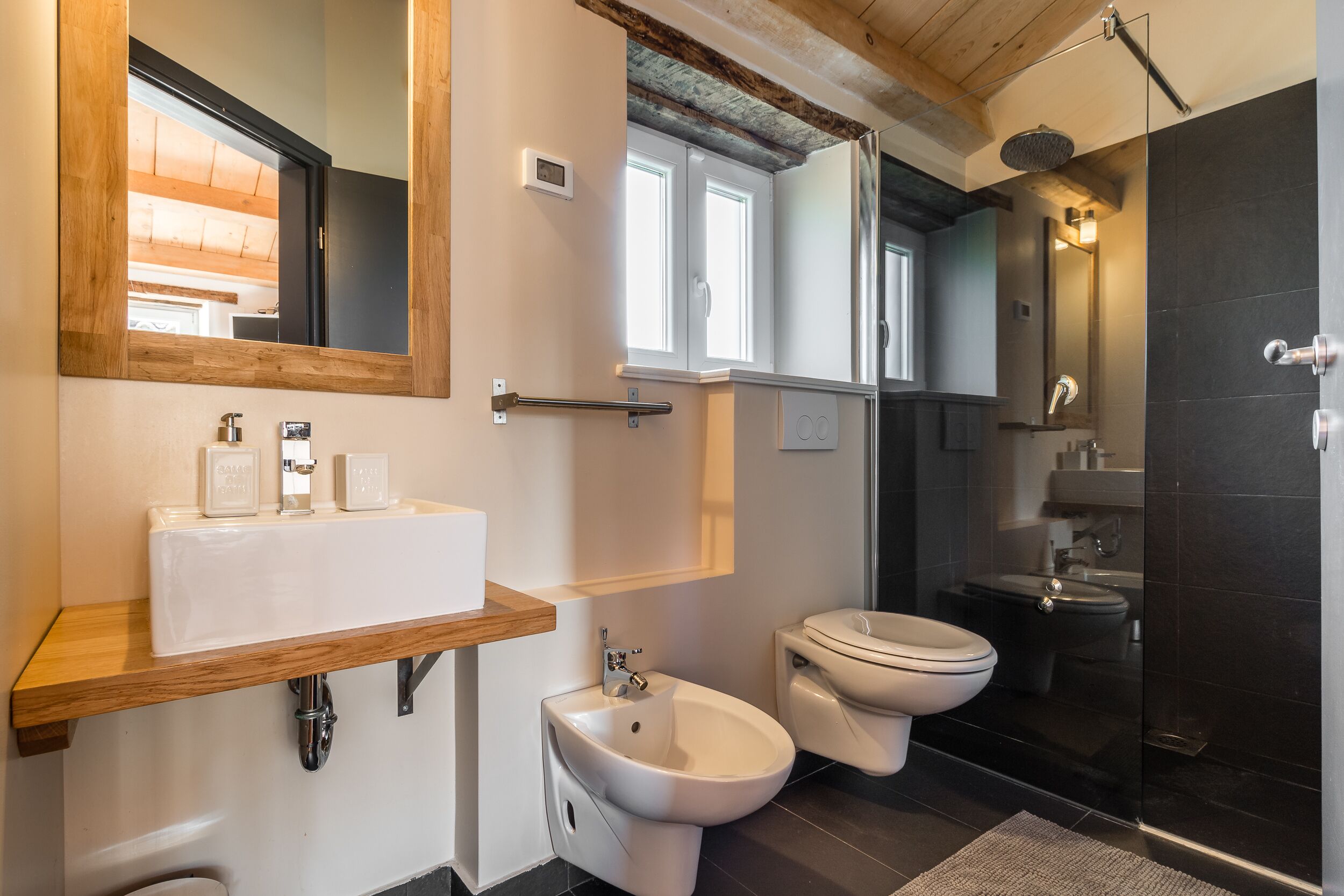 A modern bathroom with a wooden vanity, a bidet, a toilet, and a glass-enclosed shower area.