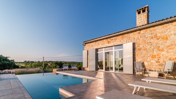 Ein Steinhaus mit Schwimmbad, Terrassenmöbeln und freiem Blick auf die umliegende Landschaft.
