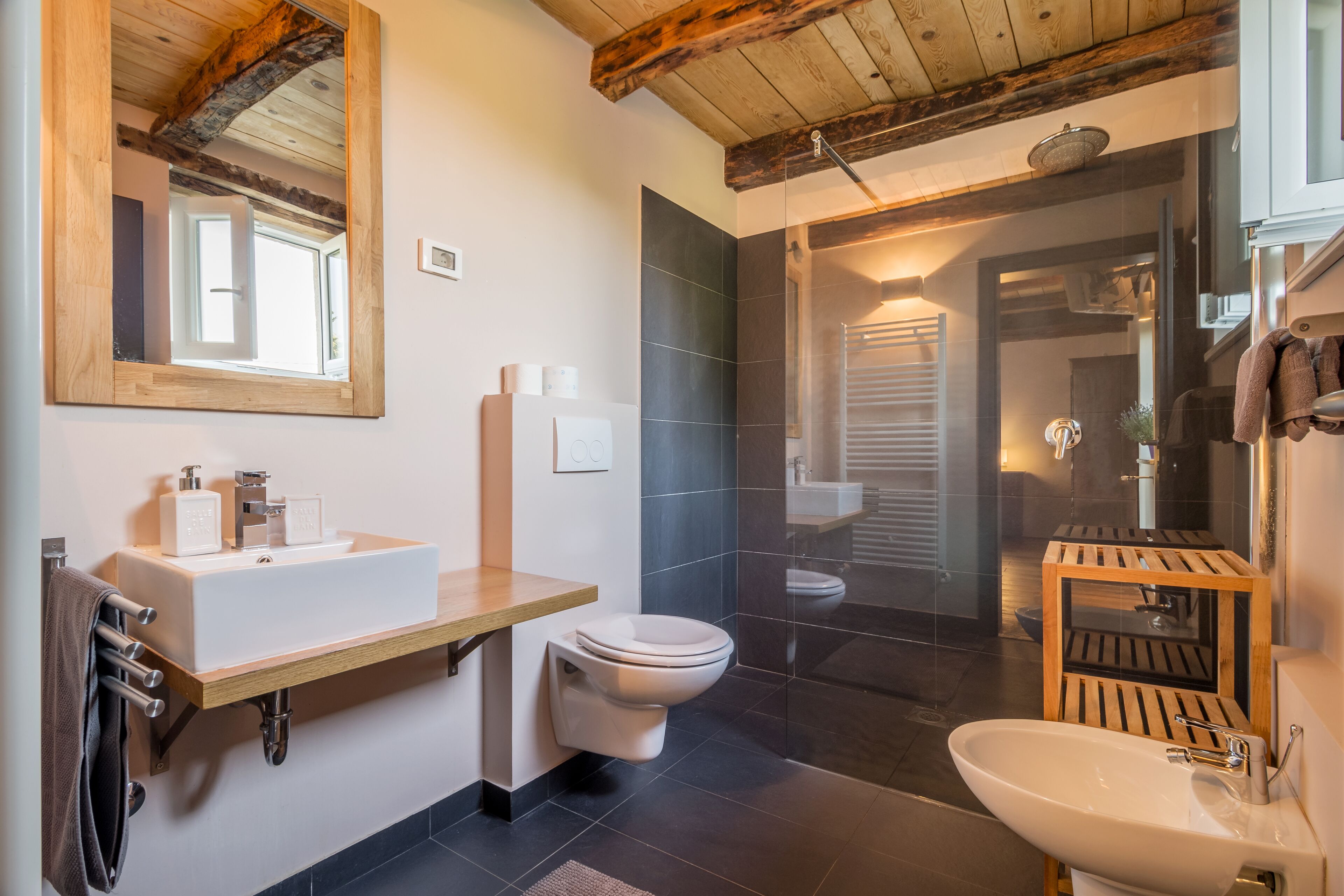 A modern bathroom with a wooden vanity, a white sink, a toilet, and a shower area.