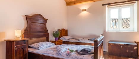 Une chambre à coucher avec un lit en bois, une table de chevet, une commode, une fenêtre donnant sur des immeubles et un plafond avec des poutres en bois.