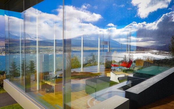 A modern room with large glass windows offering a view of a lake, mountains, and a cityscape.