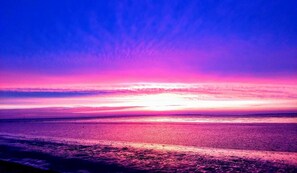 A beach at sunset with a clear sky and calm sea.