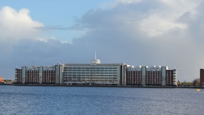 A large, modern building with a central glass facade, situated by a body of water. - Wilhelmshaven Südstrand: Hochw. Duplex apartment right on South Beach (Wilhelmshaven)