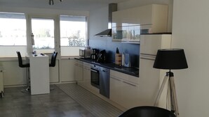 A modern kitchen with a built-in oven, microwave, and coffee maker. There is a bar area with stools and a lamp. - Wilhelmshaven Südstrand: Hochw. Duplex apartment right on South Beach (Wilhelmshaven)
