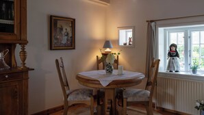 A dining area with a wooden table, chairs, a vase with flowers, a lamp, and a window with a view of a garden.