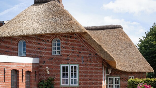 A traditional brick house with a thatched roof, a bench, and a garden.