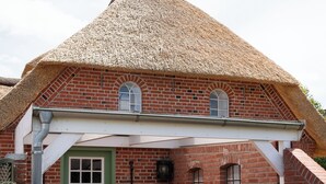 A brick building with a thatched roof, a green door, and a covered patio area with a table and chairs.