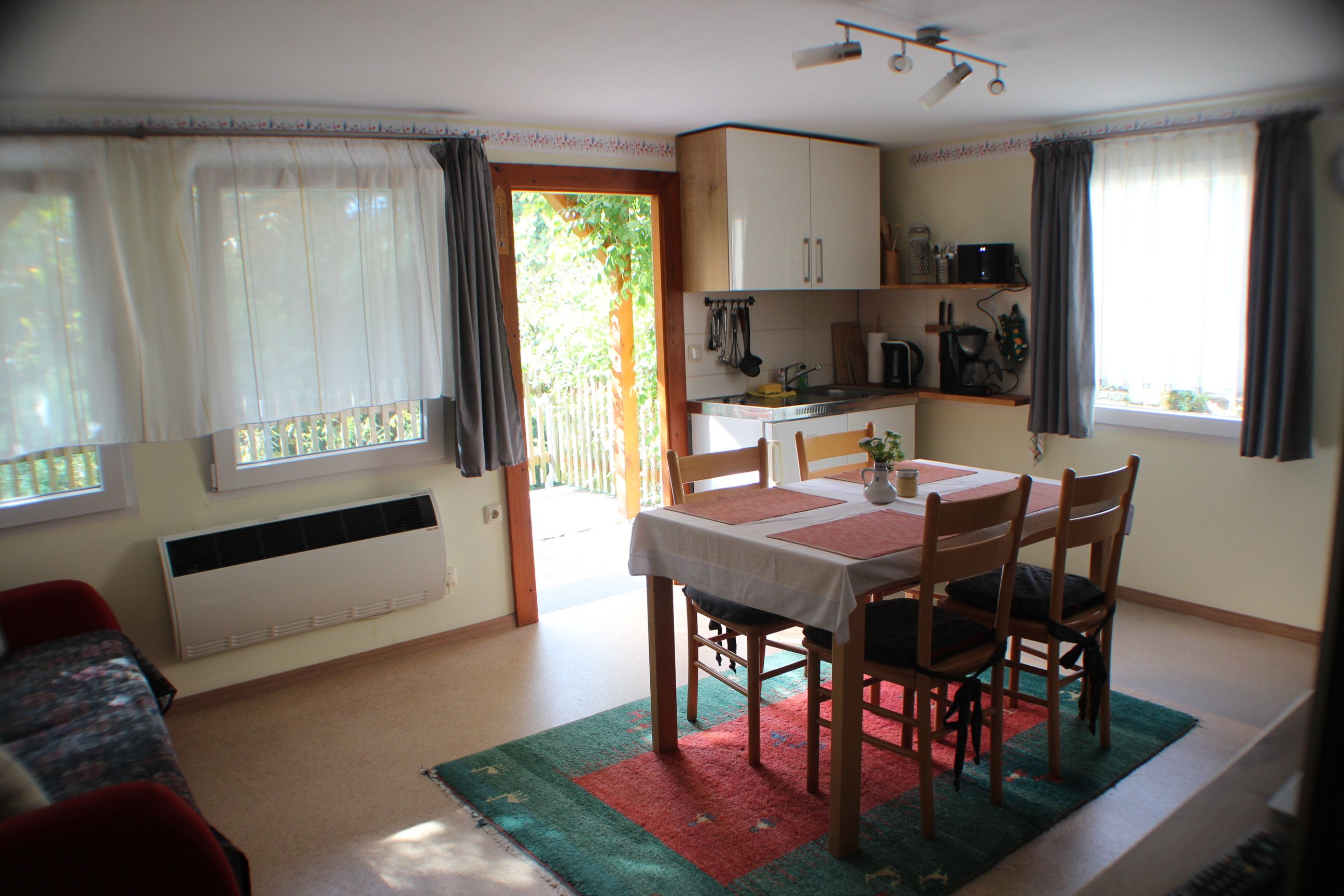 A compact room with a dining table, chairs, a kitchenette, and a window with curtains.