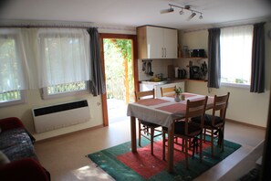 A compact room with a dining table, chairs, a kitchenette, and a window with curtains. - Vacation home on the Malerweg with pool, Saxon Switzerland, National Park (Lohmen)