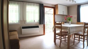 A compact kitchen with a dining table and chairs, a radiator, and a window with curtains. - Vacation home on the Malerweg with pool, Saxon Switzerland, National Park (Lohmen)