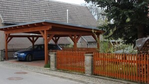 A covered parking area with a car parked inside, a wooden fence, and a stone wall. - Vacation home on the Malerweg with pool, Saxon Switzerland, National Park (Lohmen)