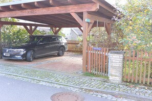 A black SUV parked under a wooden pergola with a stone wall and a wooden fence. - Vacation home on the Malerweg with pool, Saxon Switzerland, National Park (Lohmen)