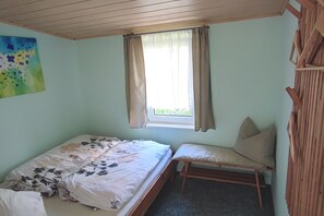 A small bedroom with a single bed, a bench, a window with curtains, and a painting on the wall. - Vacation home on the Malerweg with pool, Saxon Switzerland, National Park (Lohmen)