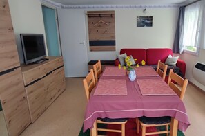 A dining area with a table set for four, a television on a wooden cabinet, and a red sofa in the background. - Vacation home on the Malerweg with pool, Saxon Switzerland, National Park (Lohmen)