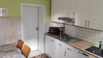 Eine kompakte Küche mit weißen Schränken, einer Mikrowelle, einer Kaffeemaschine und einem Geschirrspüler.