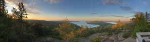 Ein Panoramablick auf eine Berglandschaft mit einem See, umgeben von dichten Wäldern und einer hölzernen Aussichtsplattform.