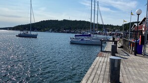 A marina with boats docked, a wooden pier, and a forested hill in the background.