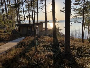 A wooden cabin with a deck, surrounded by dense forest and overlooking a body of water. - House on Hummel Bay in front of the archipelago and Skuleskogen National Park, High Coast (Köpmanholmen)