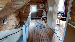 A wooden interior with a staircase leading to a second floor, a ceiling fan, and a view into an adjacent room.