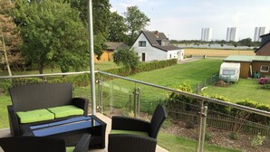 Ein Balkon mit Korbmöbeln, Blick auf eine Rasenfläche und ein weißes Haus im Hintergrund.
