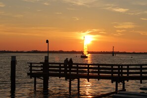 Ein Sonnenuntergang über ruhigem Wasser mit einem hölzernen Steg und einem Boot in der Ferne.