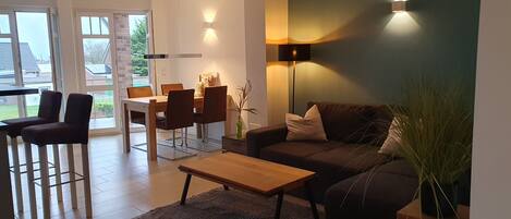 A modern living room with a sofa, a coffee table, and a dining area with chairs and a table.