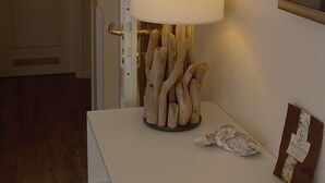 Una habitación con un escritorio blanco, una lámpara con pantalla blanca y un cuadro en la pared.
