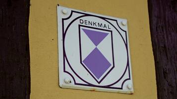 Ein Schild mit dem Wort 'DENKMAL' an einer gelben Wand mit dunklem Braunton im unteren Bereich.