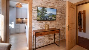 A modern living room with a stone wall, a mounted TV, and a wooden console table. - Apartment with seaview, 2 bedrroms. own garden, 5 min. to lake (Tirol)