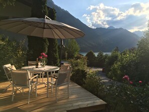 En træterrasse med et rundt bord, stole, en parasol og en vase med blomster.