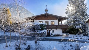 A traditional chalet with a wooden balcony, a snow-covered landscape, and a mountain in the background. - Apartment with seaview, 2 bedrroms. own garden, 5 min. to lake (Tirol)