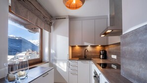 A modern kitchen with white cabinets, a wooden countertop, a built-in oven, and a window overlooking a snowy mountain. - Apartment with seaview, 2 bedrroms. own garden, 5 min. to lake (Tirol)