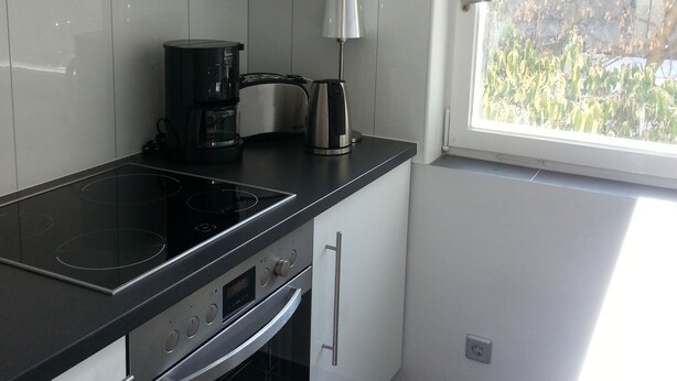 A modern kitchen with a black stove, white cabinets, and a window overlooking greenery.