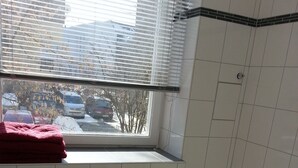 A bathroom with a toilet, a bathtub, a window with blinds, and a red towel on the windowsill.